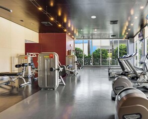 Ein Fitnessraum mit Cardiogeräten, Gewichten und großen Fenstern mit Blick ins Freie.