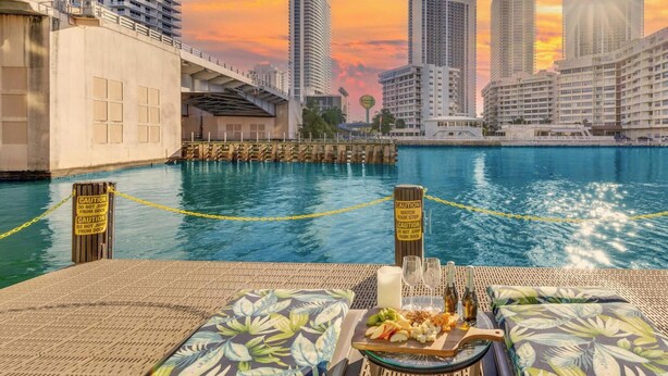 A waterfront dining area with a view of the city skyline, a dock, and caution signs. - Intracoastal View Apt | Balcony & Beach Shuttle (Hallandale Beach)