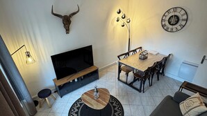 Sala de estar com sofá, televisão, mesa de jantar e um relógio decorativo na parede.