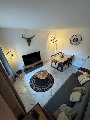Ein Wohnzimmer mit einer Couch, einem Fernseher, einem Esstisch und einer Wanduhr.