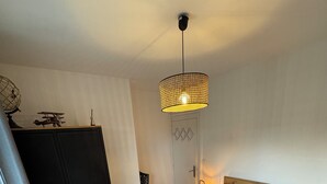 Quarto com cama, guarda-roupa, porta e luminária suspensa.