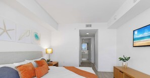 A hotel room with a bed, a nightstand, a lamp, a TV, and a plant. - Sunset View-Bright Apt- Bay View & Private Balcony (Hallandale Beach)