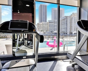A gym with exercise equipment and a large window with a city view. - Upper-Floor Studio | Balcony, Sleeps 4 (Hallandale Beach)