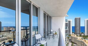 Ein Balkon mit Blick auf Stadt und Meer, ausgestattet mit modernen Stühlen und einem kleinen Tisch.