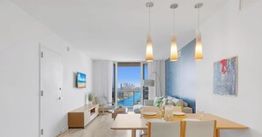 Ein modernes Wohnzimmer mit Essbereich, großen Fenstern und Blick auf die Stadt, sparsam eingerichtet.