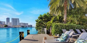 A waterfront balcony with lounge chairs, a pool, and a city skyline in the background. - Marina Views  2BR  Beachwalk Resort (Hallandale Beach)