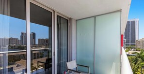 Un balcon donnant sur une vue de la ville, une chaise et une table avec une bouteille et un verre.