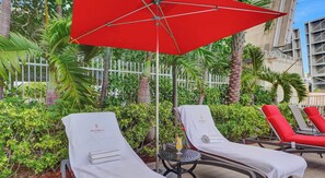 Ein Poolbereich mit Liegestühlen, einem roten Sonnenschirm und einem Tisch mit einem Getränk.