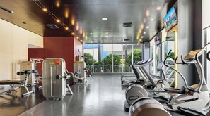 A gym with cardio machines, weight training equipment, and a large window providing a view of the outdoors. - Waterway View 2BR · Beachwalk Resort (Hallandale Beach)