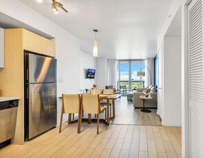 A modern kitchen with a stainless steel refrigerator, dining table with chairs, and a TV mounted on the wall. - Waterway View 2BR · Beachwalk Resort (Hallandale Beach)