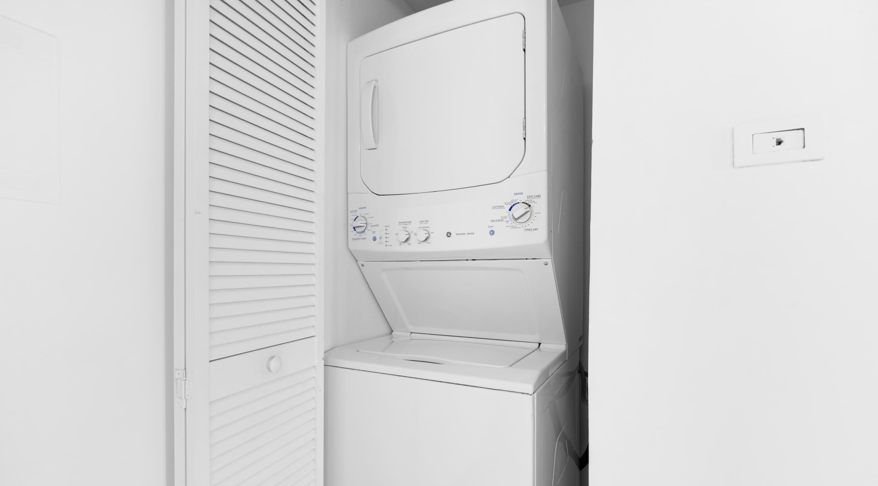 A white washing machine with control panel, a white wall, and a door with horizontal blinds.