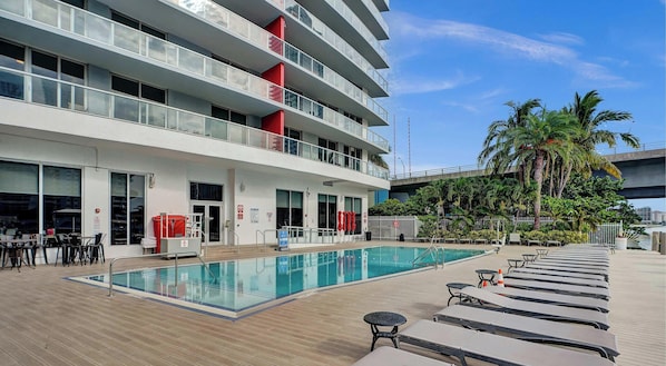 A hotel with a swimming pool, outdoor seating, and a view of palm trees. - Spacious BW - 1BR APT - Resort‑Style experience (Hallandale Beach)