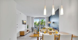 A modern dining area with a wooden table, white chairs, and pendant lights. - Stunning 1BR · Gym & Resort Pool (Hallandale Beach)