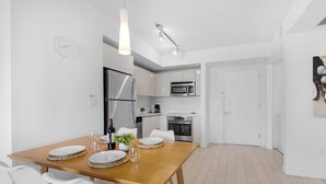 A modern kitchen with stainless steel appliances, a dining table set for four, and a white interior. - Stunning 1BR · Gym & Resort Pool (Hallandale Beach)