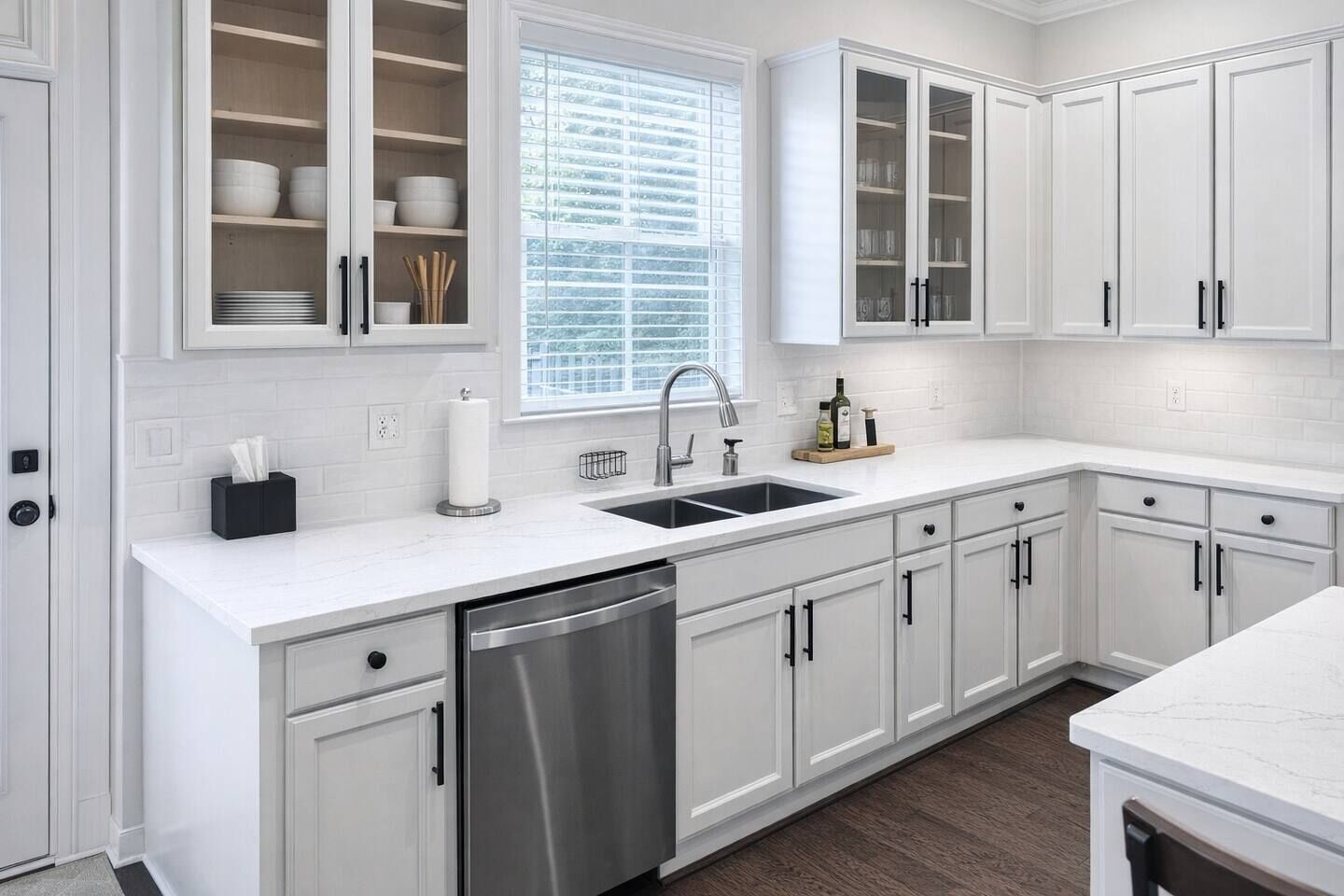 A modern kitchen with white cabinetry, a stainless steel dishwasher, a double sink, and a window with blinds.