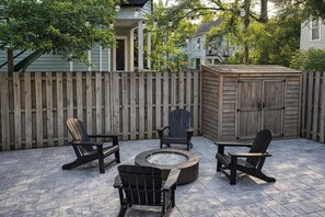 Eine Terrasse mit Feuerstelle, drei Adirondack-Stühlen und einem Holzschuppen.