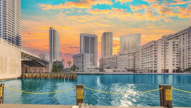 Ein Speisebereich am Wasser mit Blick auf die Skyline der Stadt, eine Anlegestelle und Warnschilder.
