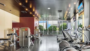 Ein Fitnessstudio mit Cardiogeräten, Krafttrainingsgeräten und einem großen Fenster mit Blick auf Grünflächen.