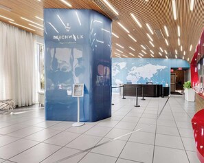 A modern hotel lobby with a curved reception desk, a world map on the wall, and a wooden ceiling design. - Bright 1BR · Bay View · Resort Amenities & Beach (Hallandale Beach)