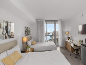 Habitación de hotel con cama, escritorio, televisión y vista a un paisaje urbano.