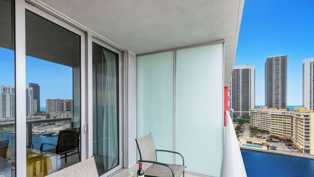 Un balcón con una silla y mesa, con vistas a un puerto deportivo y al paisaje urbano.