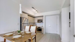 Eine moderne Küche mit Edelstahlgeräten, ein Essbereich mit einem Holztisch, gedeckt für vier Personen, und eine weiße Tür, die in einen weiteren Raum führt.