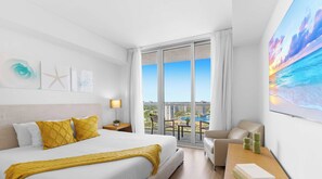 Ein Hotelzimmer mit einem großen Bett, einem Schreibtisch, einem Sessel und Blick auf Stadt und Wasser.