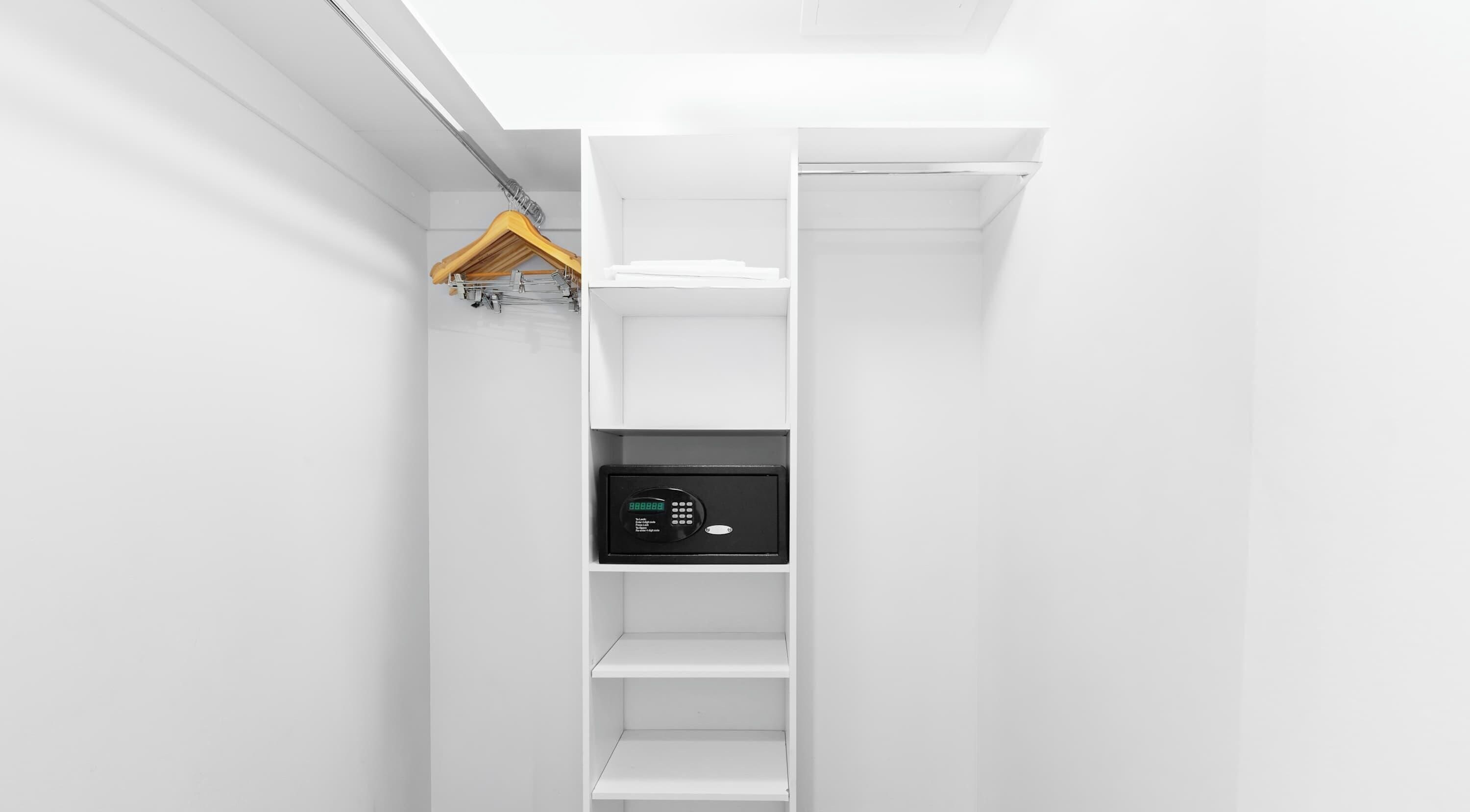Ein weißer Kleiderschrank mit Kleiderstange und einem schwarzen Safe.