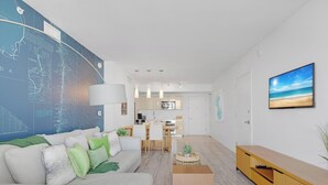 En moderne stue med sofa, sofabord og spiseområde med et køkken i baggrunden.