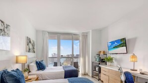 Habitació d'hotel amb dos llits, un escriptori amb un ordinador, una televisió i vista a la ciutat.