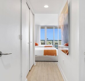 Ein modernes Hotelzimmer mit Balkon, großem Fenster und einem Bett mit orangefarbener Bettwäsche.