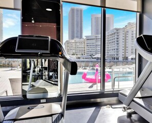 A gym with exercise equipment and a large window with a city view. - Stylish Studio w/ Intracoastal View & Gym (Hallandale Beach)