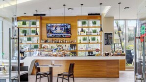 Uma área de bar moderna com balcão de madeira, diversas opções de assento e uma tela de televisão acima do balcão.