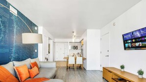 Uma sala de estar moderna com um grande mapa na parede, um sofá com almofadas laranja, uma área de jantar com mesa de madeira e uma cozinha com armários brancos.
