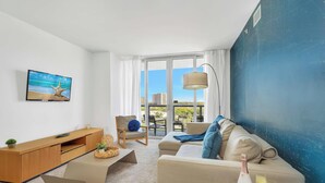 Ett modernt vardagsrum med en tv, en soffa, ett soffbord och utsikt över staden genom stora fönster.