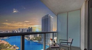 A balcony with a city view, a table with a bottle and glasses, and a chair. - Elegant 2BR Condo · Beachwalk Resort Pool (Hallandale Beach)