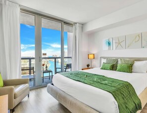 A hotel room with a large bed, two bedside lamps, a view of the city, and a balcony. - Bay & City View 2BR · Beachwalk High Floor (Hallandale Beach)