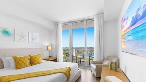 A hotel room with a bed, a chair, a table, and a large window with a city view. - New! Bay & City View 2BR - Beachwalk High Floor (Hallandale Beach)