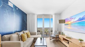A modern living room with a sofa, coffee table, and a view of the city through large windows. - New! Bay & City View 2BR - Beachwalk High Floor (Hallandale Beach)