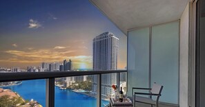 A balcony with a city view, a table with a bottle and glasses, and a chair. - Bay & City View 2BR · Beachwalk High Floor (Hallandale Beach)