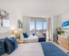 Een moderne hotelkamer met een bed, nachtkastje, lamp en stadszicht door grote ramen.