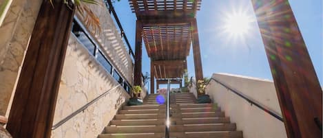 Un escalier menant à un espace abrité agrémenté d’une pergola, entouré de murs en pierre et de plantes en pot.