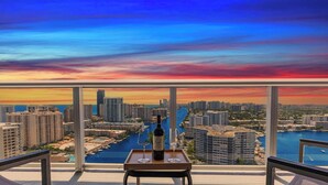 Un balcon avec vue sur la ville au coucher du soleil, une bouteille de vin et deux verres à vin sur un plateau.