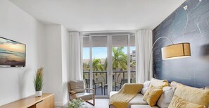 Una sala de estar moderna con un sofá, una silla, un televisor, una planta y un balcón con vistas.