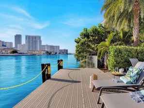 Um deck à beira-mar com espreguiçadeiras, piscina e o horizonte da cidade ao fundo.