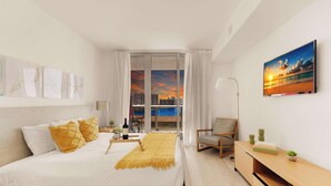 Habitación de hotel moderna con cama, una silla, un escritorio y un amplio ventanal con vista a la ciudad.