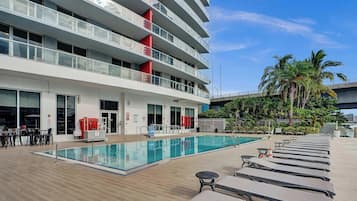 Área de piscina de hotel com vista desobstruída, cadeiras de descanso e um edifício com varandas múltiplas.