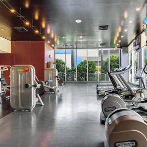 Ein Fitnessraum mit Cardiogeräten, Gewichten und großen Fenstern mit Blick ins Freie.