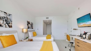 Ein Hotelzimmer mit zwei Betten, einem Schreibtisch, einem Stuhl, einem Fernseher und Bildern an den Wänden.