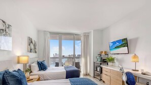 Habitación de hotel con dos camas, un escritorio con computadora, televisor y vista a la ciudad.